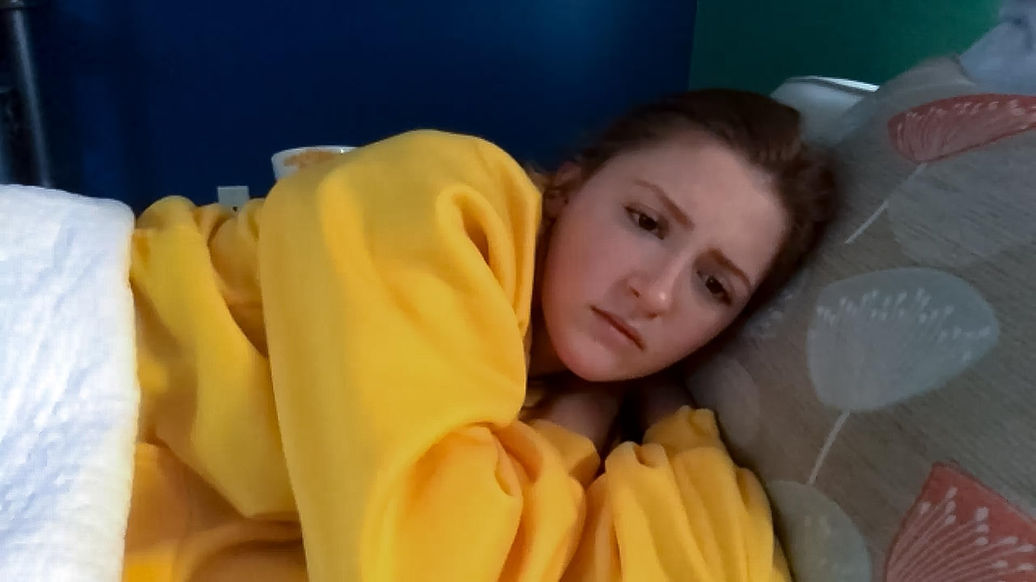 A young woman in a yellow sweater lies in a bed
